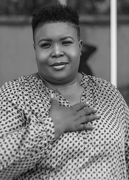 image of a woman smiling. her hand is up on her chest and she is looking at the camera.